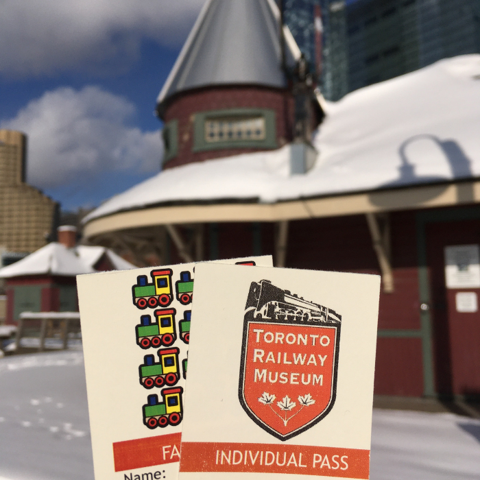 Also on the gift guide, annual passes. Two paper passes are held in front of a snow-covered train station outdoors.