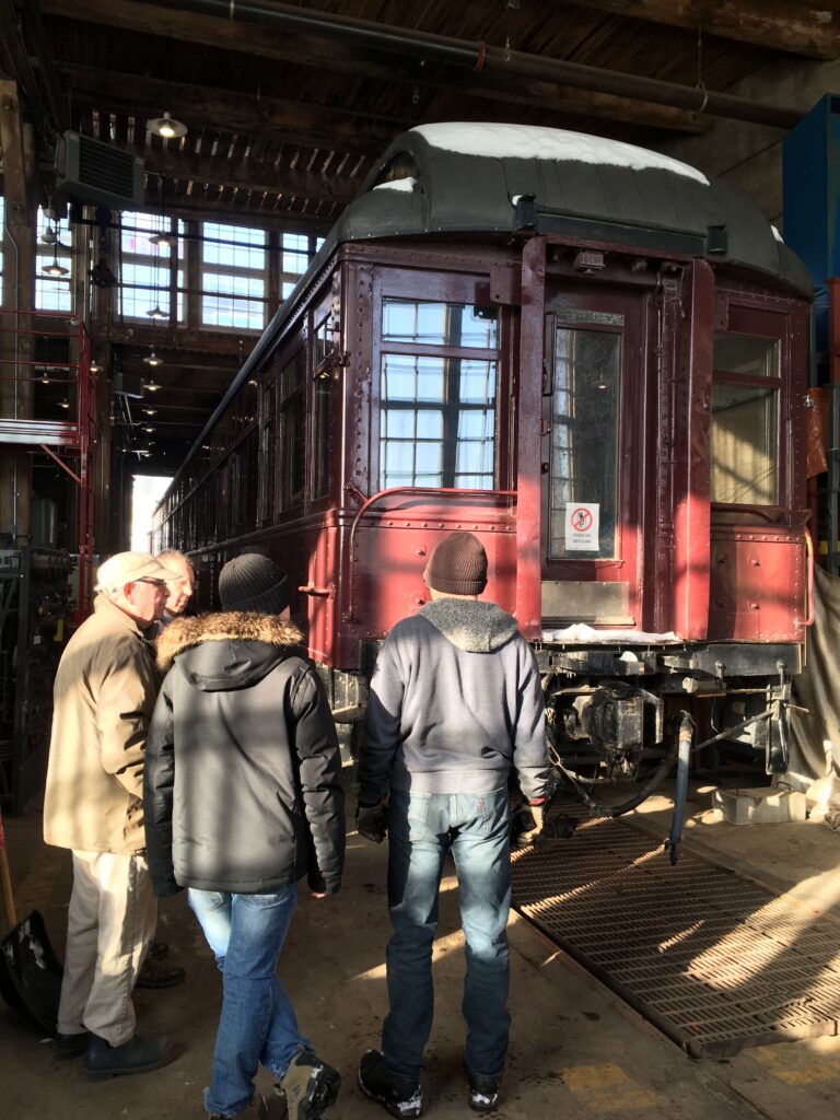 Volunteers stand in Stall 15 of the Roundhouse looking at Cape Race. They have just moved the car into the restoration area.