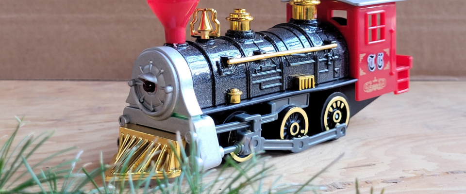 model toy train is posed against a plain brown background. Fresh greenery peeks into the foreground.