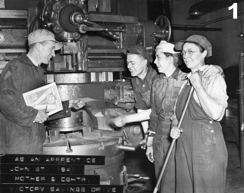 1941 photo of two women and two men in front of machinery inside the Roundhouse. John Clarke is reaching to grab a war bond from General Foreman Bob Scott. Everyone is dressed in coveralls and work clothes.