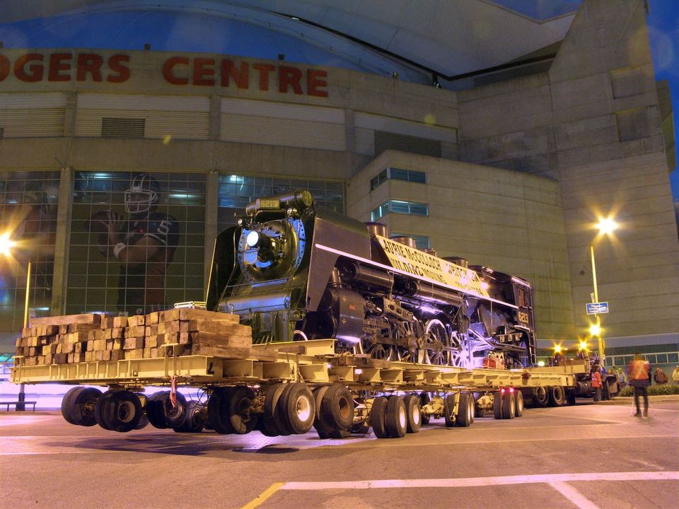 6213 and trailer making a tight turn in front of the Rogers Centre. The locomotive is the  main focus but you can see the sports arena in the background.