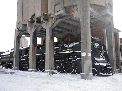 6213 is under the coaling tower at the museum, partially obscured by the tower's support beams. Snow on the ground.