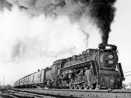 Black and white photograph of number 6213. The locomotive is hauling a train and has a big plume of dark smoke coming out of the top.
