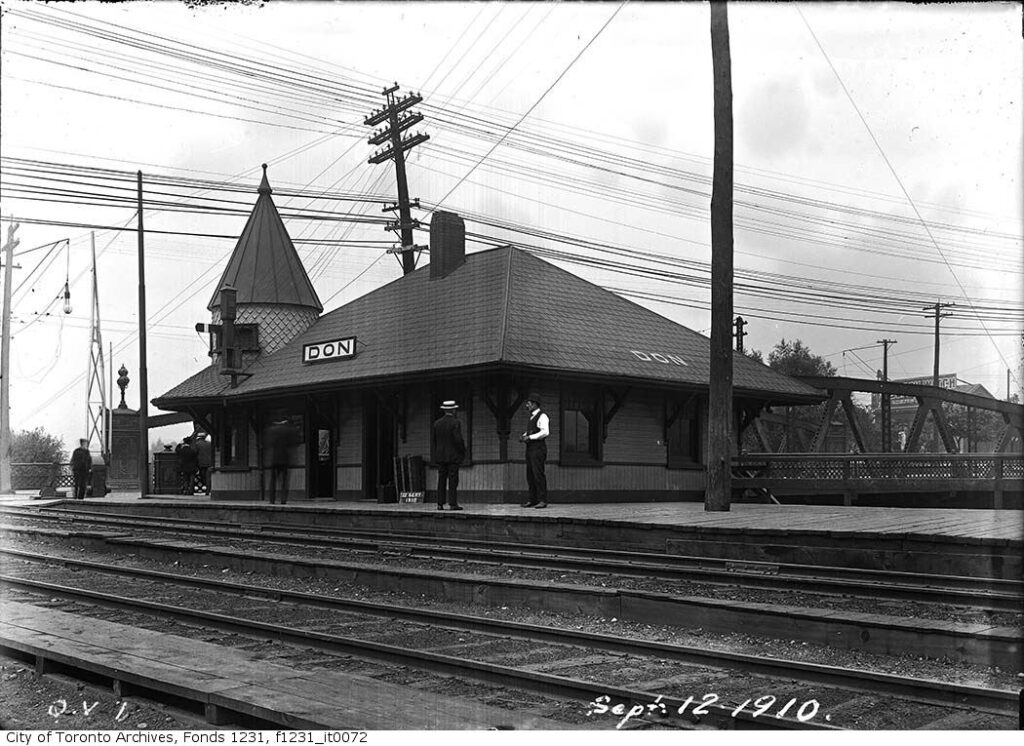 Black and white historical photo of Don Station taken at track level. There are five men standing on the station's platform, one wears a boater-style hat, another is only in white shirtsleeves.