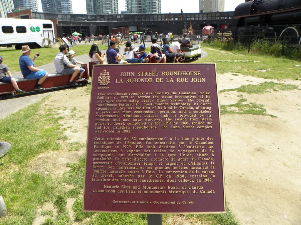 A red plaque with gold text sits outside at the Toronto Railway Museum proclaiming the JOhn Street Roundhouse a National Historic Site.