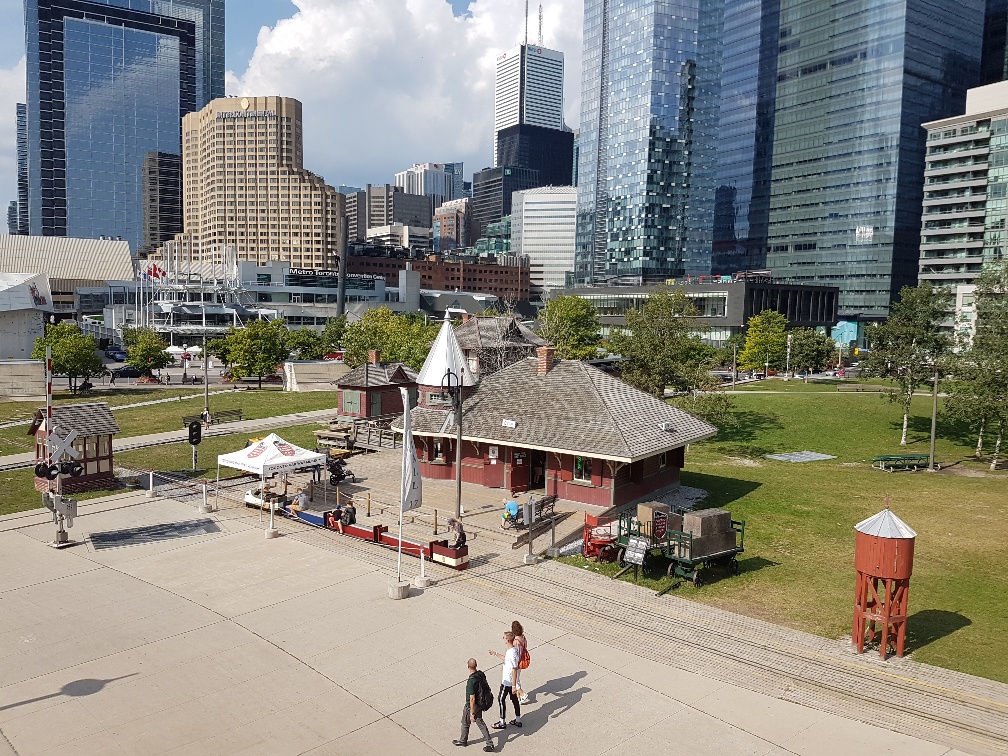 View of Don Station from above. The miniature train ride is parked on the platform and visitors to the museum mill about the park on a sunny summer day.