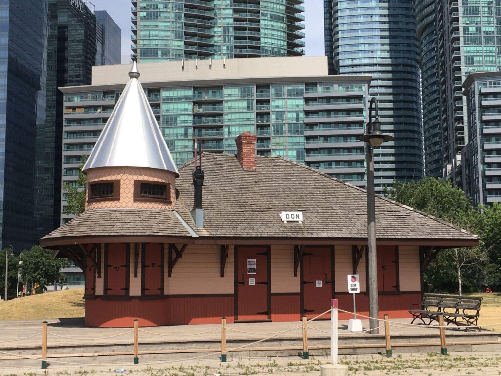 Don Station painted in a crimson red with light pinky beige accents on the body of the building. It is a sunny day and the metal of the station's turret glints in the sun.