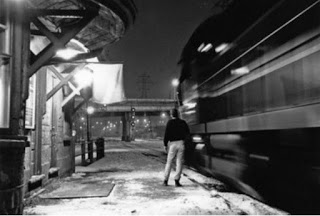 Black and white historical photo of Don Station taken on the platform with John Mellow's back to us. Next to him, a train rolls past the station which looks blurry in the photo because of the movement.