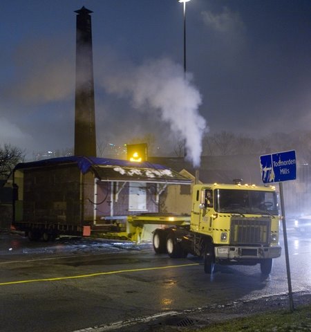 Nighttime photo of a semi truck pulling the main station building of Don Station. It is a wet, December night and the truck's headlights reflect off the wet road.