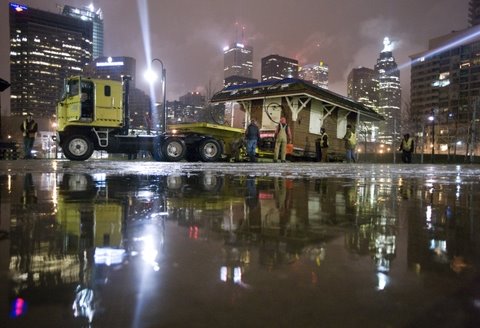 Nighttime photo of Don Station being dropped off at the Toronto Railway Museum. City lights and the truck's headlights reflect off the wet road.