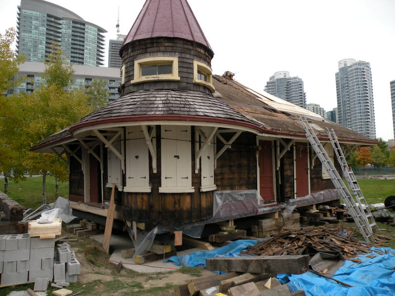 Don Station's restoration continued. The station has been mostly stripped of paint leaving a natural wood tone showing through. The station rests on wooden blocks, awaiting a foundation and two ladders lean against the roof.