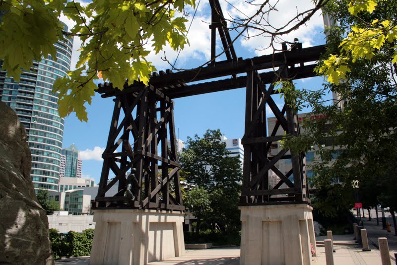 A sculpture of a railway trestle bridge is raised on concrete plinths. Greenery from nearby trees peek into the photo.
