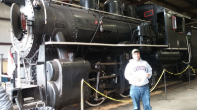 A man posed in front of a black steam locomotive.