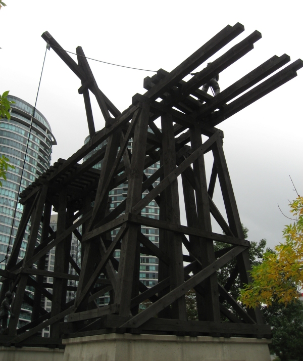 Side view of the sculpture of a railway trestle bridge is raised on concrete plinths on a cloudy day.