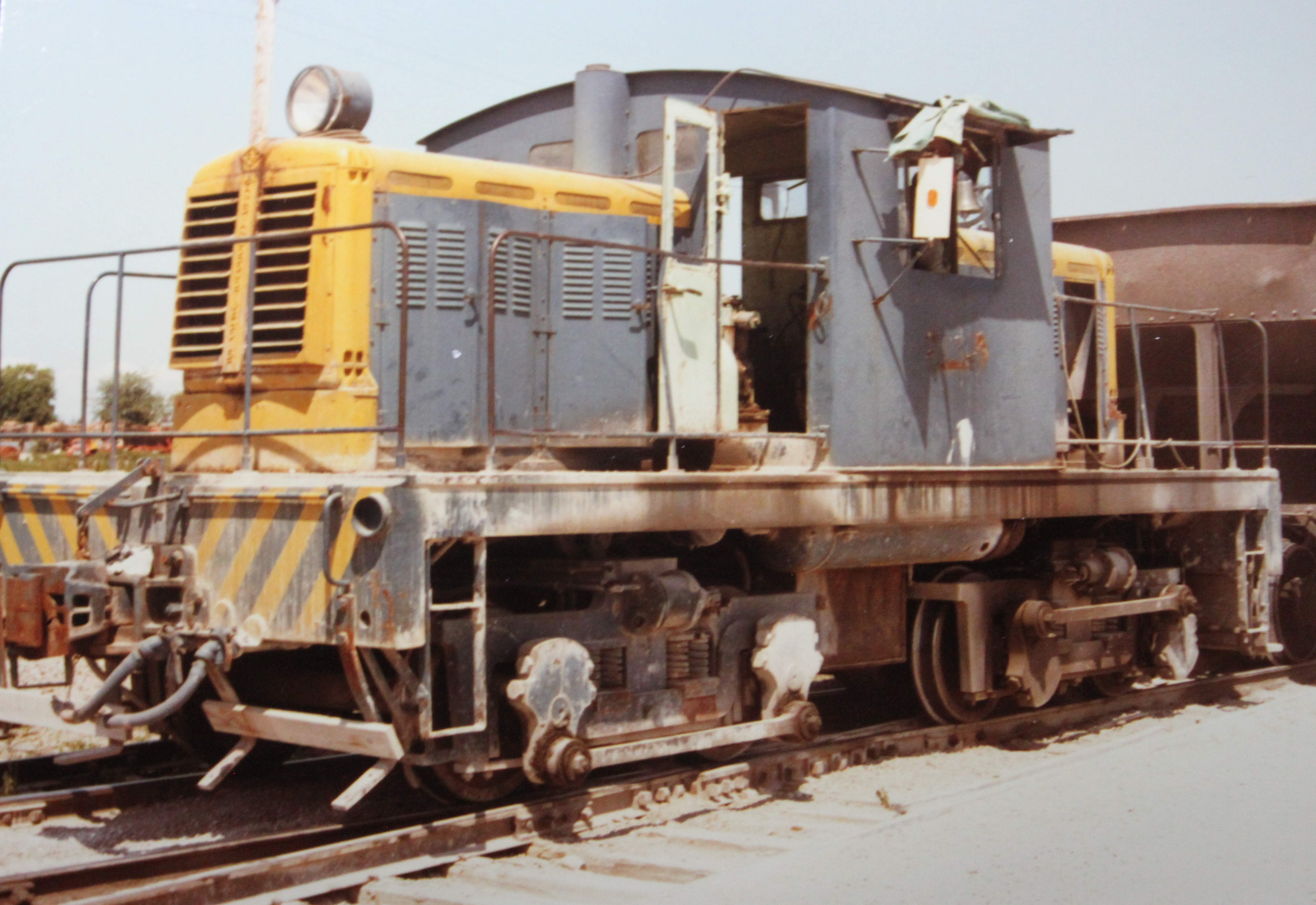 No. 1 is connected to a brown hopper car in an industrial environment. The door to the locomotive cab is ajar.