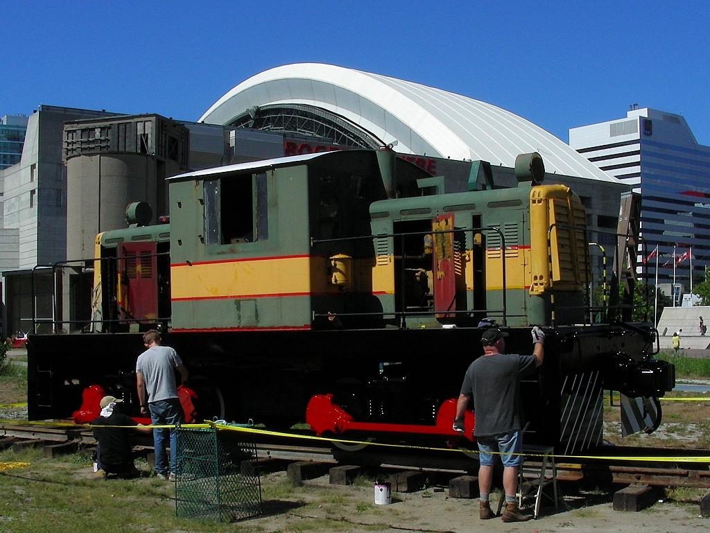 three volunteers work on No. 1 on the museum grounds. Two volunteers look at the wheels and rods of the locomotive; Another volunteer is painting a section of No. 1.