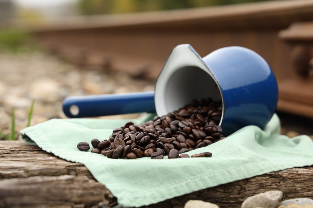 Close up photo of coffee beans artfully spilt on a pale blue cloth, which is resting on a weathered wooden railway tie.