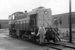 A locomotive engineer wearing coveralls poses on the front of a diesel locomotive.