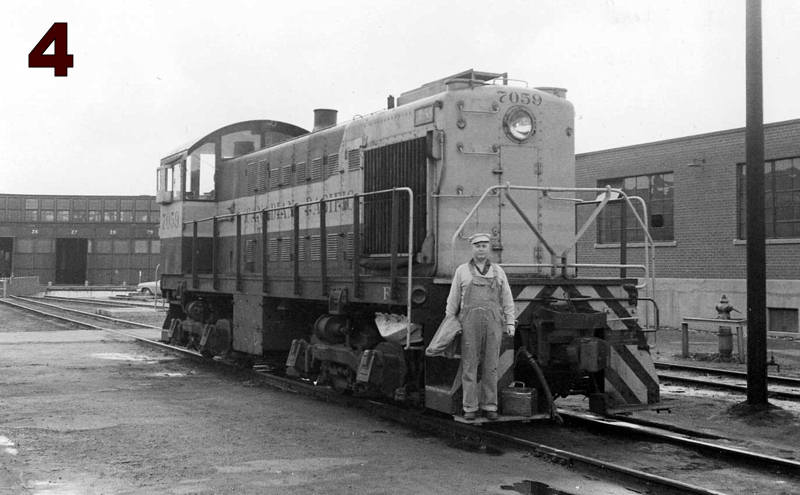 A man wearing coveralls poses on the front of a diesel locomotive.