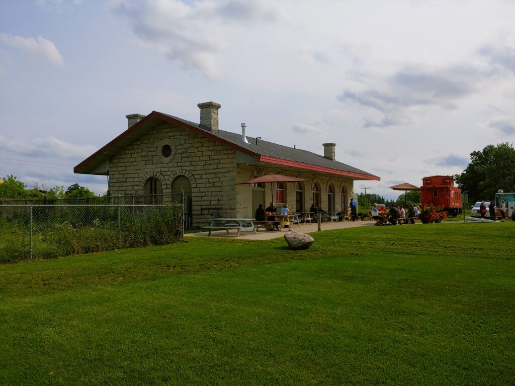 A low, single-level train station with a patio that has two umbrellas on it.