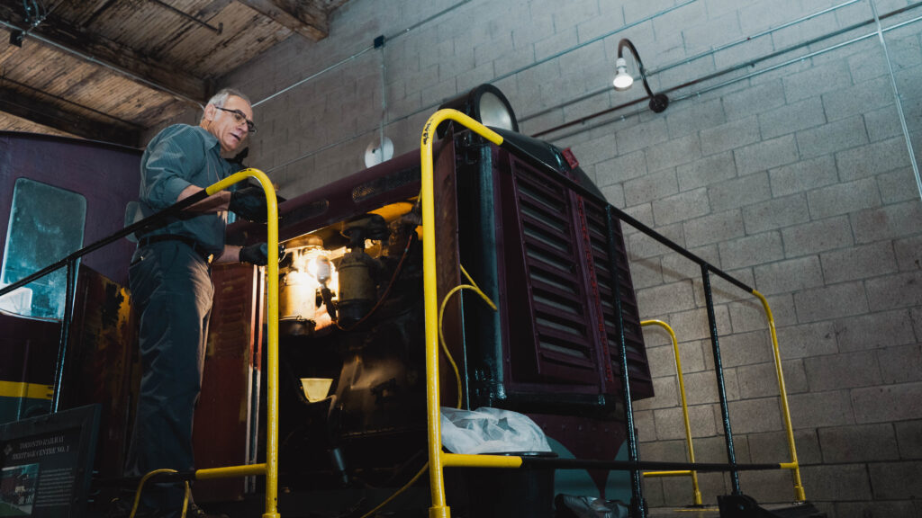 Museum staff person stands on top of a diesel locomotive working on the engine